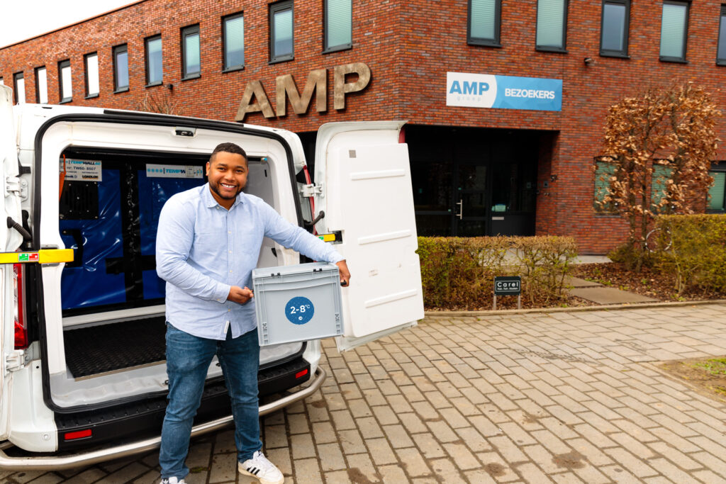 Glimlachende bezorger van AMP Groep die voor de geconditioneerde bezorging van medicijnen, een passieve koelbox met temperatuurvermelding uit een witte koelwagen laad.